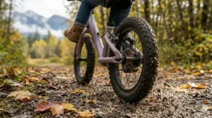 Low-angle shot of rugged, knobby tires on a purple balance bike with a hand brake, gripping a damp, leaf-covered gravel path in a Canadian provincial park.