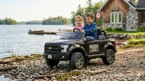 A photorealistic 4K image showing kids playing with a black 12V toy Ford F-150-style truck with a 'CANADA' license plate and a weathered 'MUSKOKA LAKEFRONT ADVENTURES' decal and a small bilingual sticker on a pebble lakefront during a sunny afternoon. A Canadian cottage and a large lake are in the background.