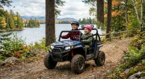 Two children sharing an all-terrain utility ride-on vehicle outdoors.