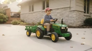 Toddler driving a 6v tractor with trailer on a smooth paved driveway.