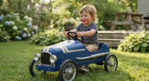 A toddler smiling while steering a durable blue metal pedal race car for kids in a backyard.