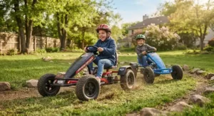 Two kids smiling while racing their off-road pedal go-karts on a grassy backyard track.
