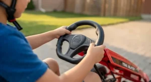 Detail shot of a child's hands gripping the responsive steering wheel of an outdoor pedal go-kart for kids.