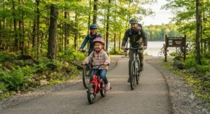 Family enjoying a weekend bicycle ride together in an Ontario provincial park with their preschooler leading the way on a first pedal bike.