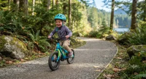 Enthusiastic preschooler riding a first pedal bike with training wheels removed on a smooth British Columbia park trail.